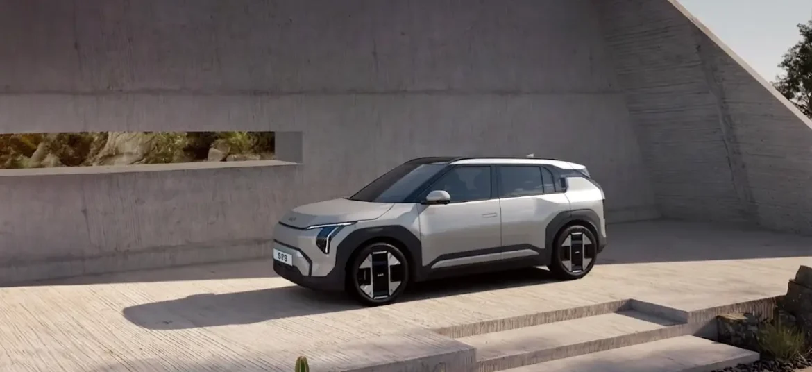 An ivory silver color kia EV3 electric suv parked infront of a box type building