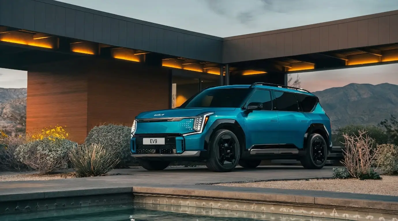 An ocean blue color kia EV9 SUV parked near a small garden near a pool