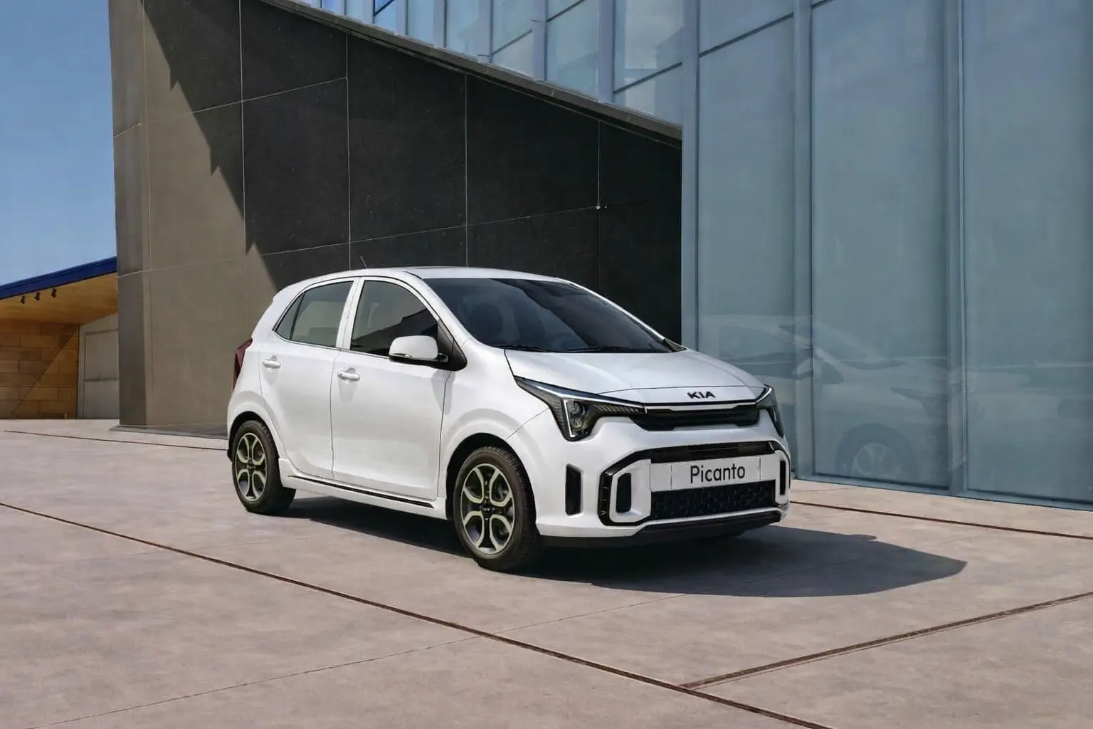 A white color picanto hatchback car parked in front of a glass wall